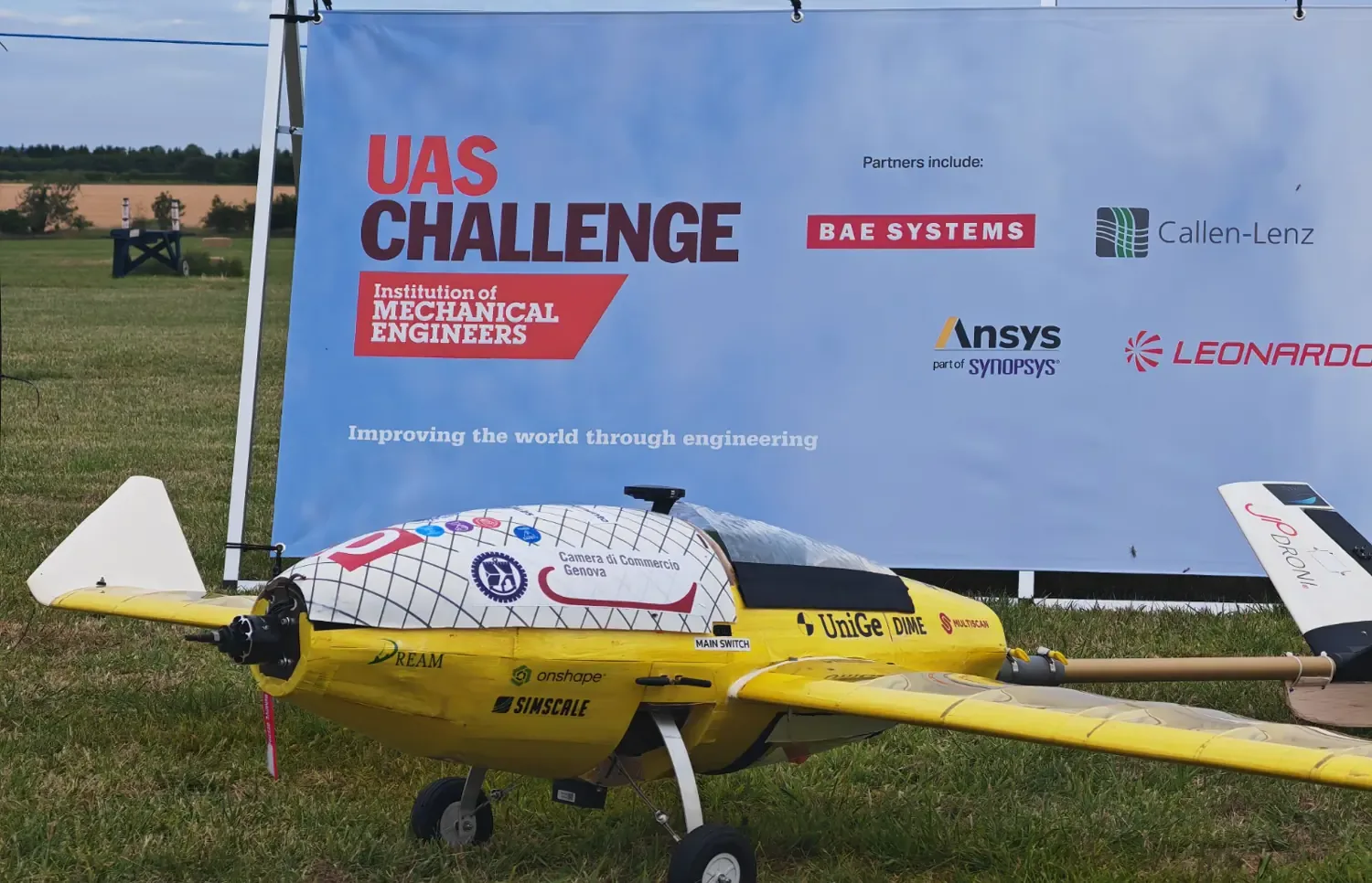 Panissa, il velivolo giallo di DOPE Hubs con impennaggio a V, sul campo della UAS Challenge davanti allo striscione dell’Institution of Mechanical Engineers.